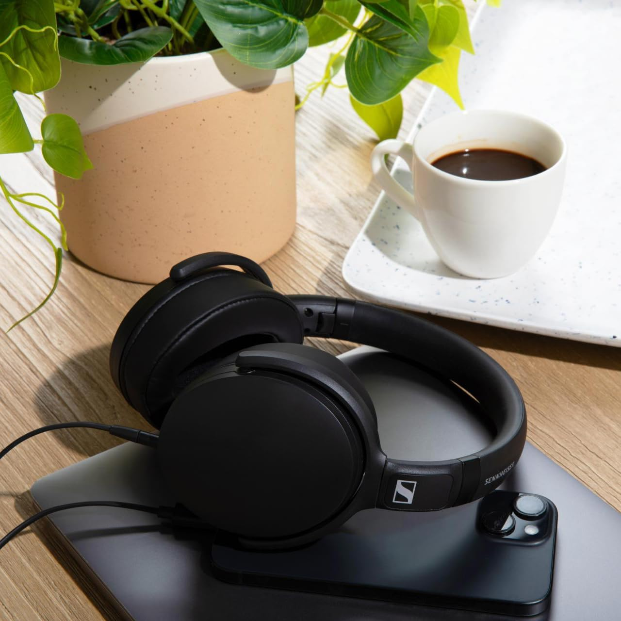 Casque noir posé sur un ordinateur portable, avec une tasse de café et une plante.