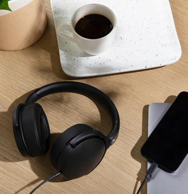 Casque noir, tasse de café, pot de plante et téléphone sur un bureau en bois.