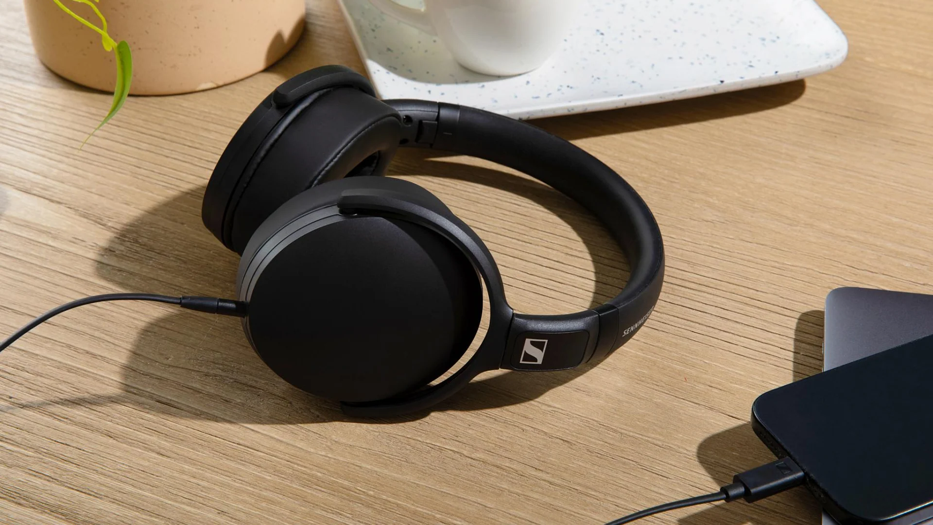 Casque noir filaire posé sur un bureau en bois à côté d'un smartphone.