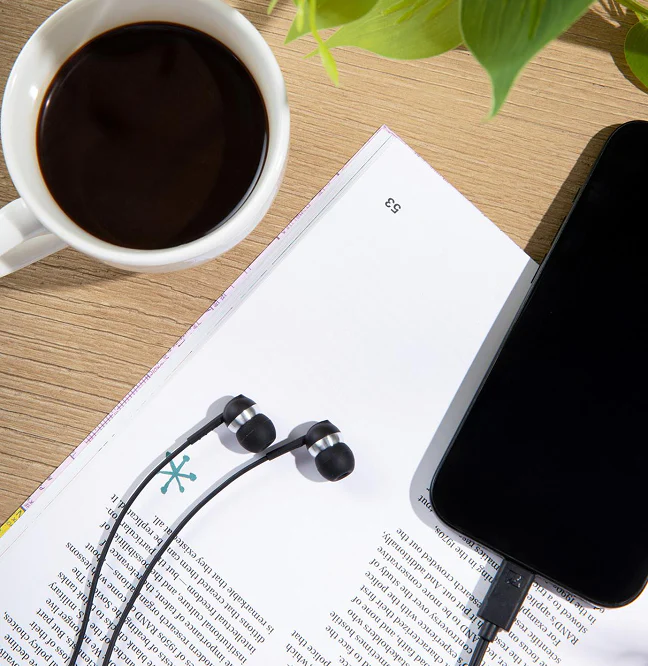 Eine Tasse Kaffee, Kopfhörer und ein Smartphone liegen auf einem Buch.