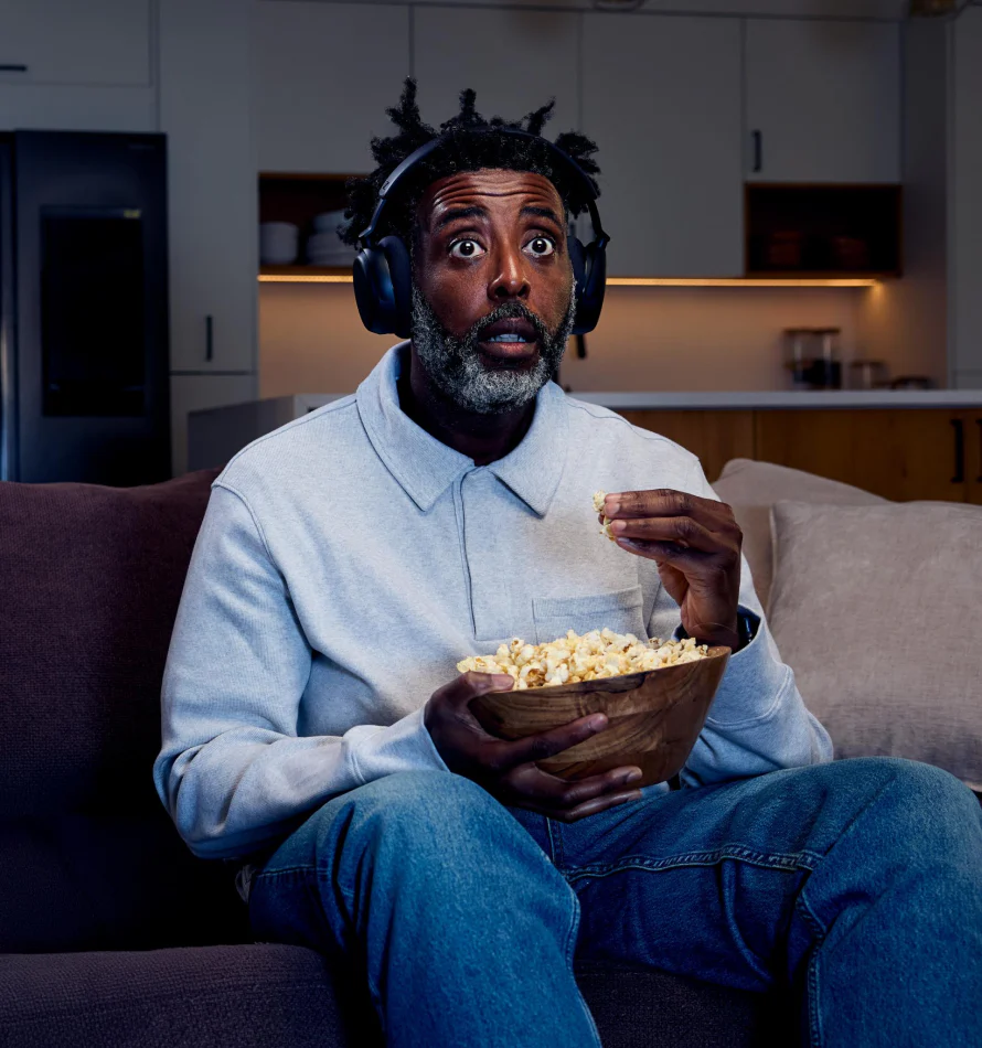 Un homme avec un casque mange du pop-corn en regardant la TV, choqué.
