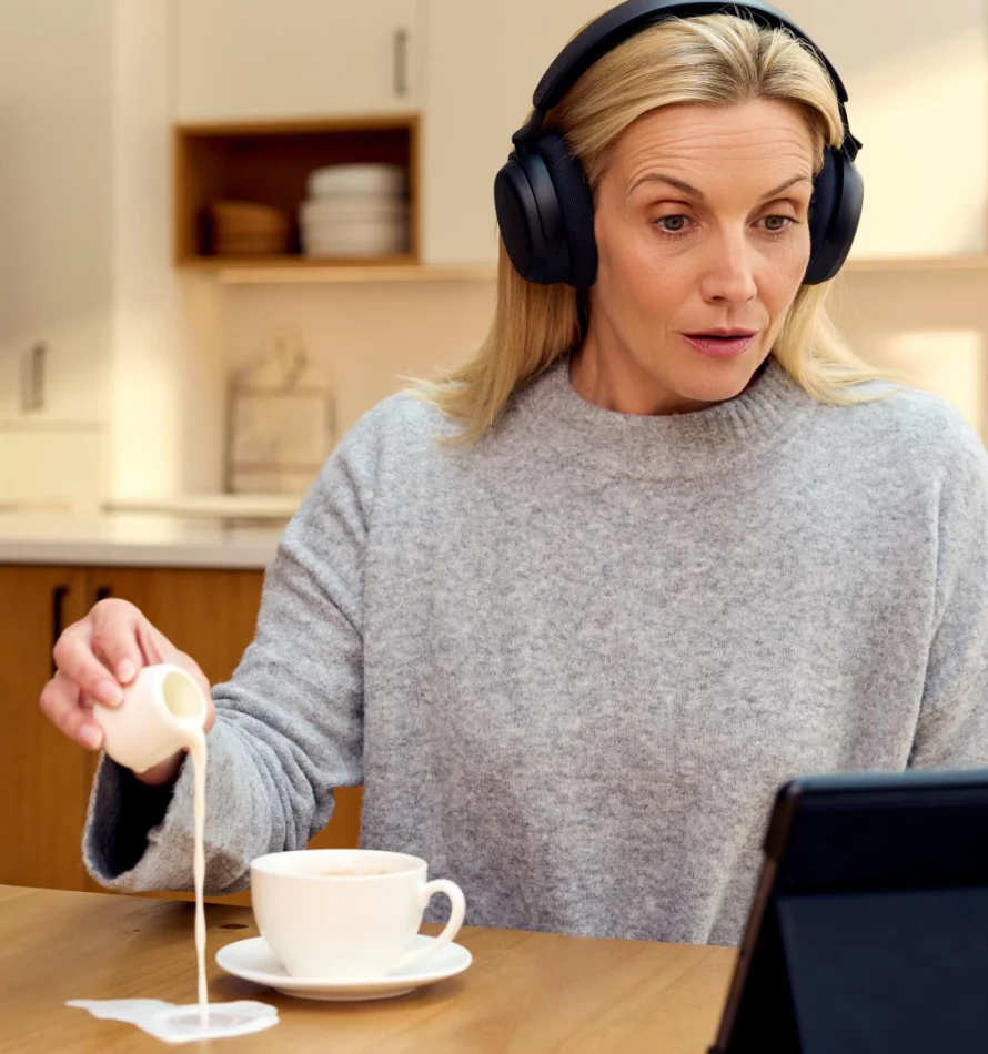 Femme avec casque verse du lait dans une tasse en regardant une tablette.