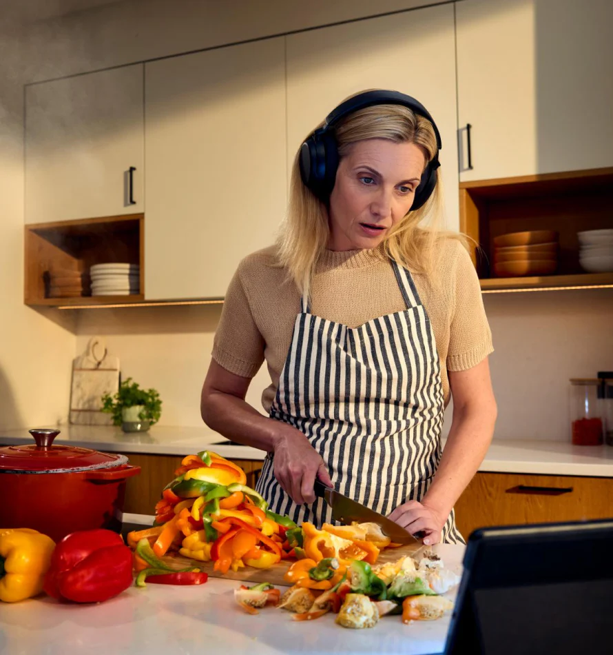 Femme avec casque coupe des poivrons dans une cuisine.