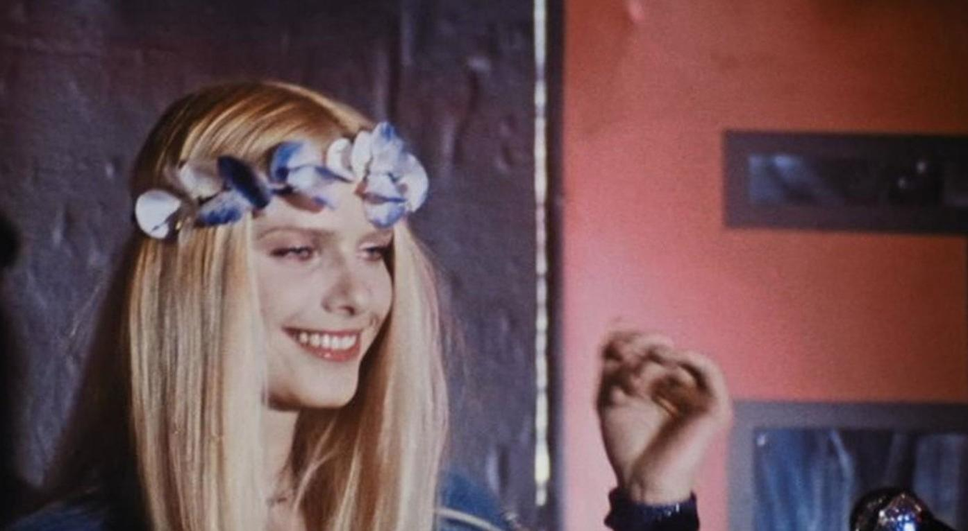 Eine Frau mit blonden Haaren und Blumenkranz lächelt.