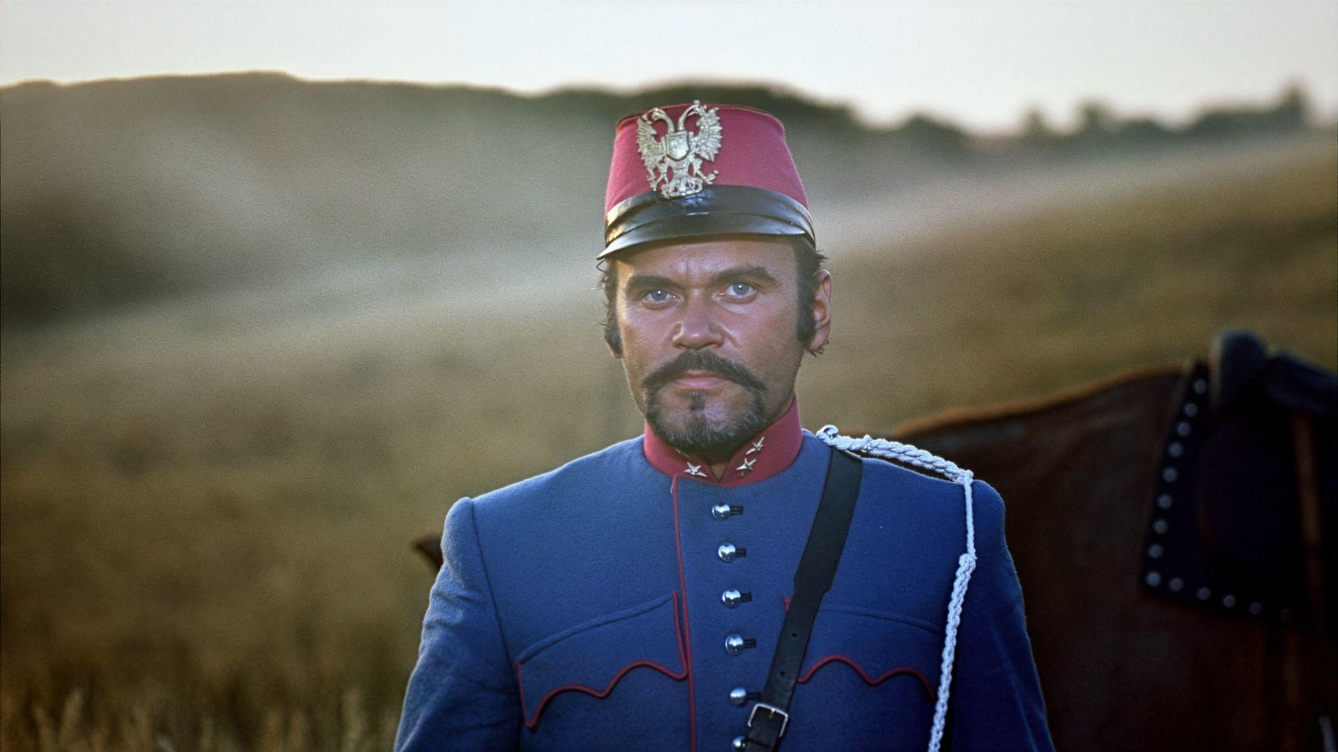 Ein Mann in einer blauen Uniform mit einem roten Hut mit Adler, im Freien.