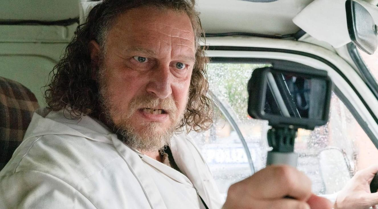 Mann mit Bart fährt Auto, Kamera im Vordergrund.