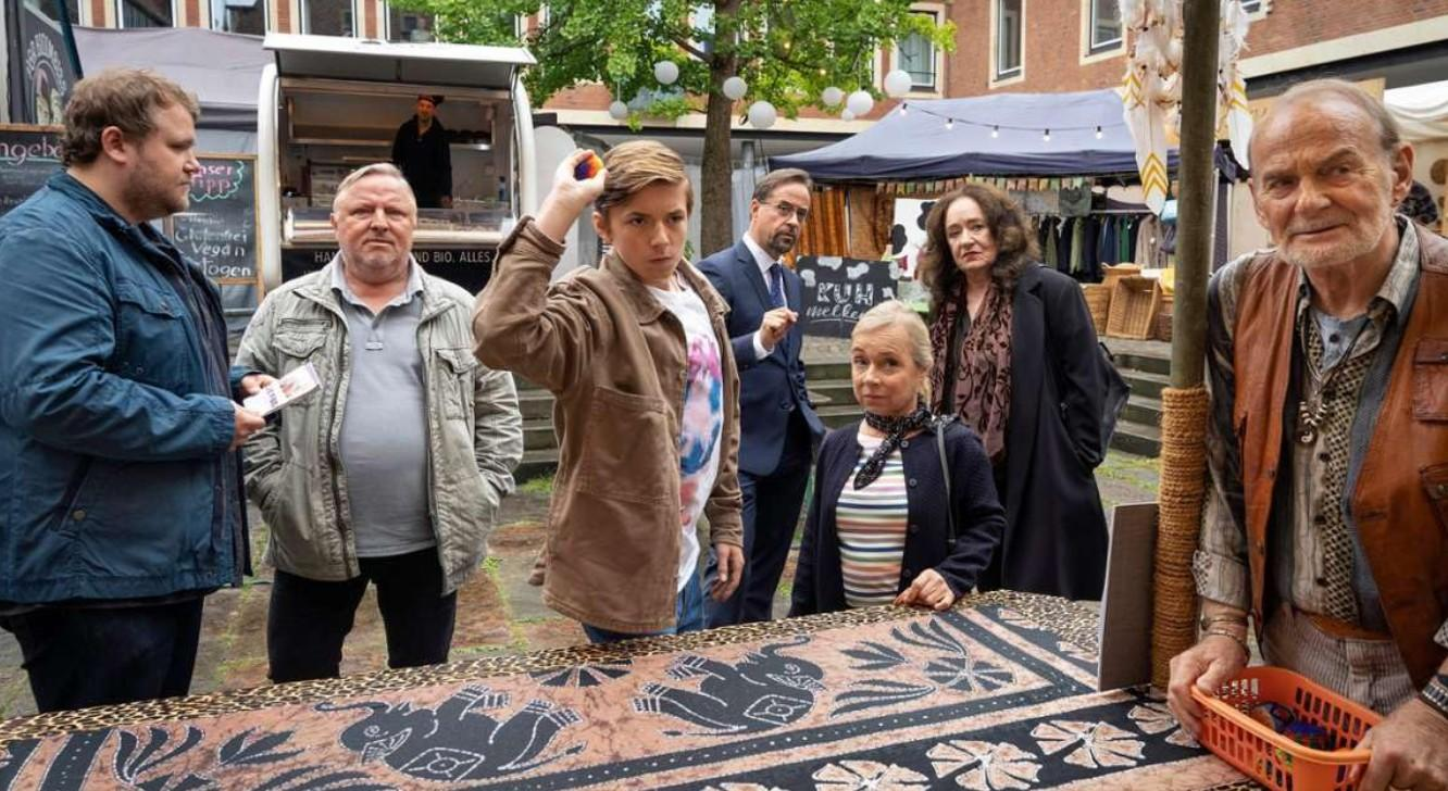 Gruppe von Menschen auf einem Markt, ein Junge wirft einen Ball, im Hintergrund ein Imbisswagen.