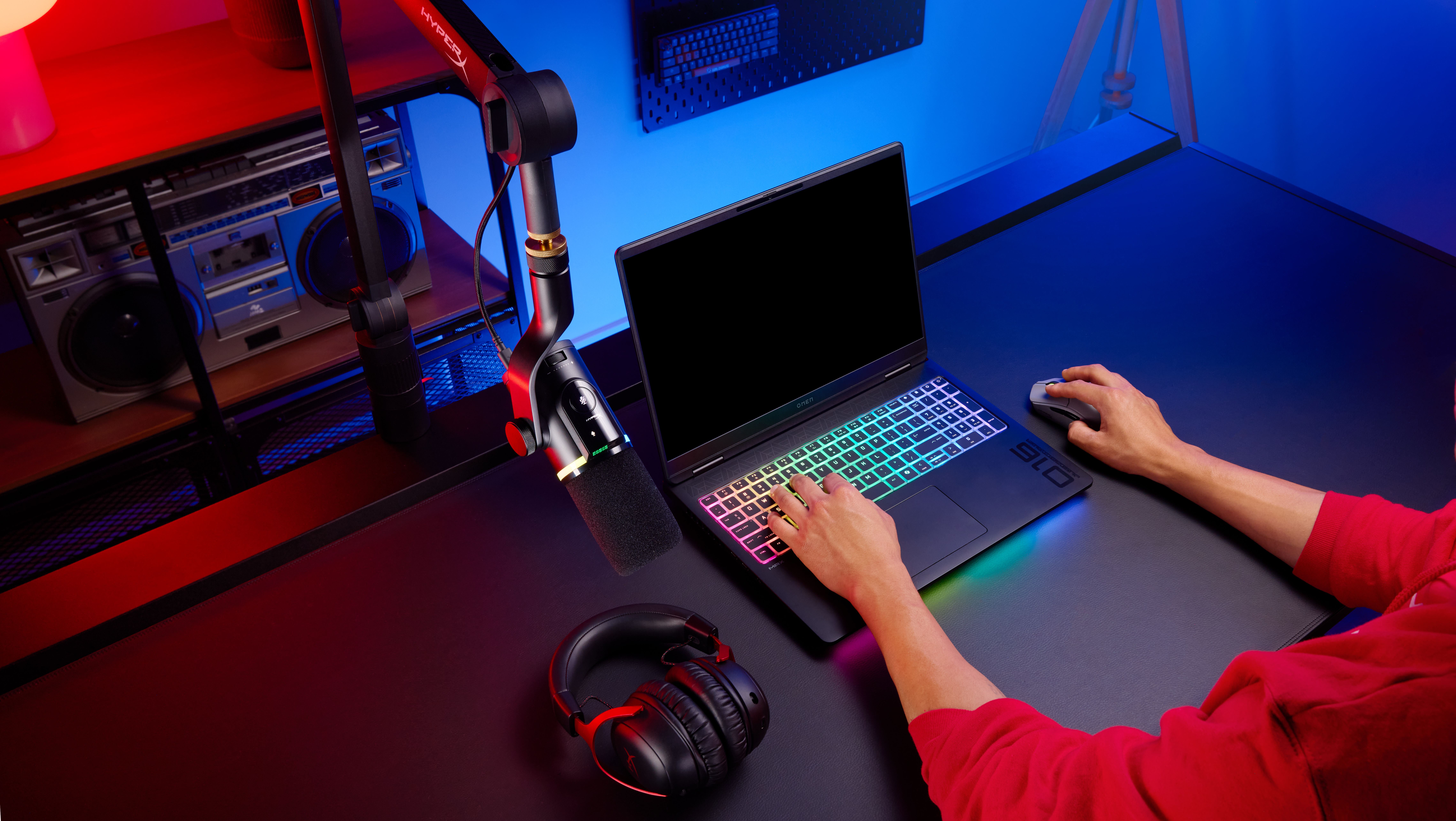 Una persona digita su un laptop con tastiera colorata, cuffie e microfono nelle vicinanze.