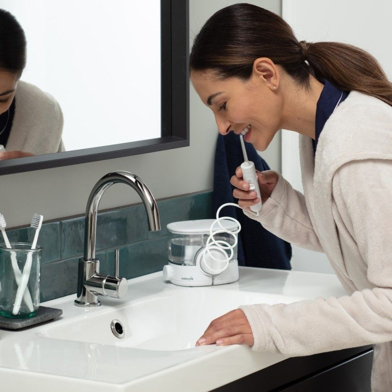 Kobieta używa irygatora w łazience przy umywalce.