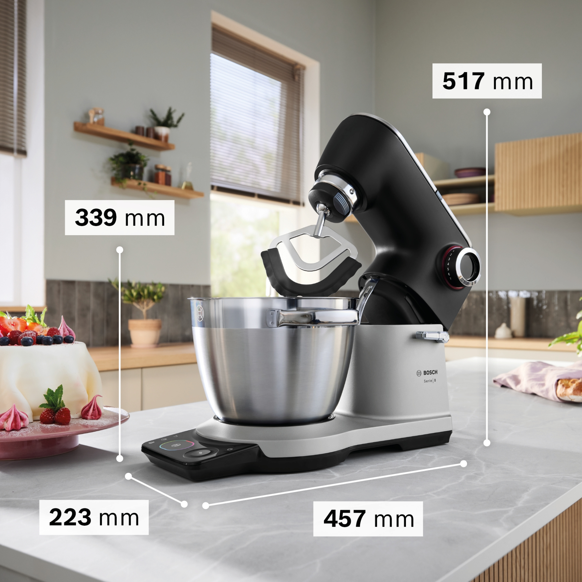 Ein schwarzer Küchenmaschinen-Mixer mit Edelstahlschüssel, daneben ein Kuchen.