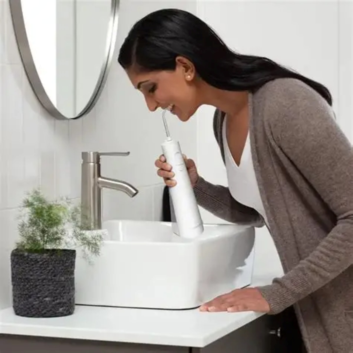 Kobieta używa białej irygatora do zębów nad umywalką do higieny jamy ustnej.