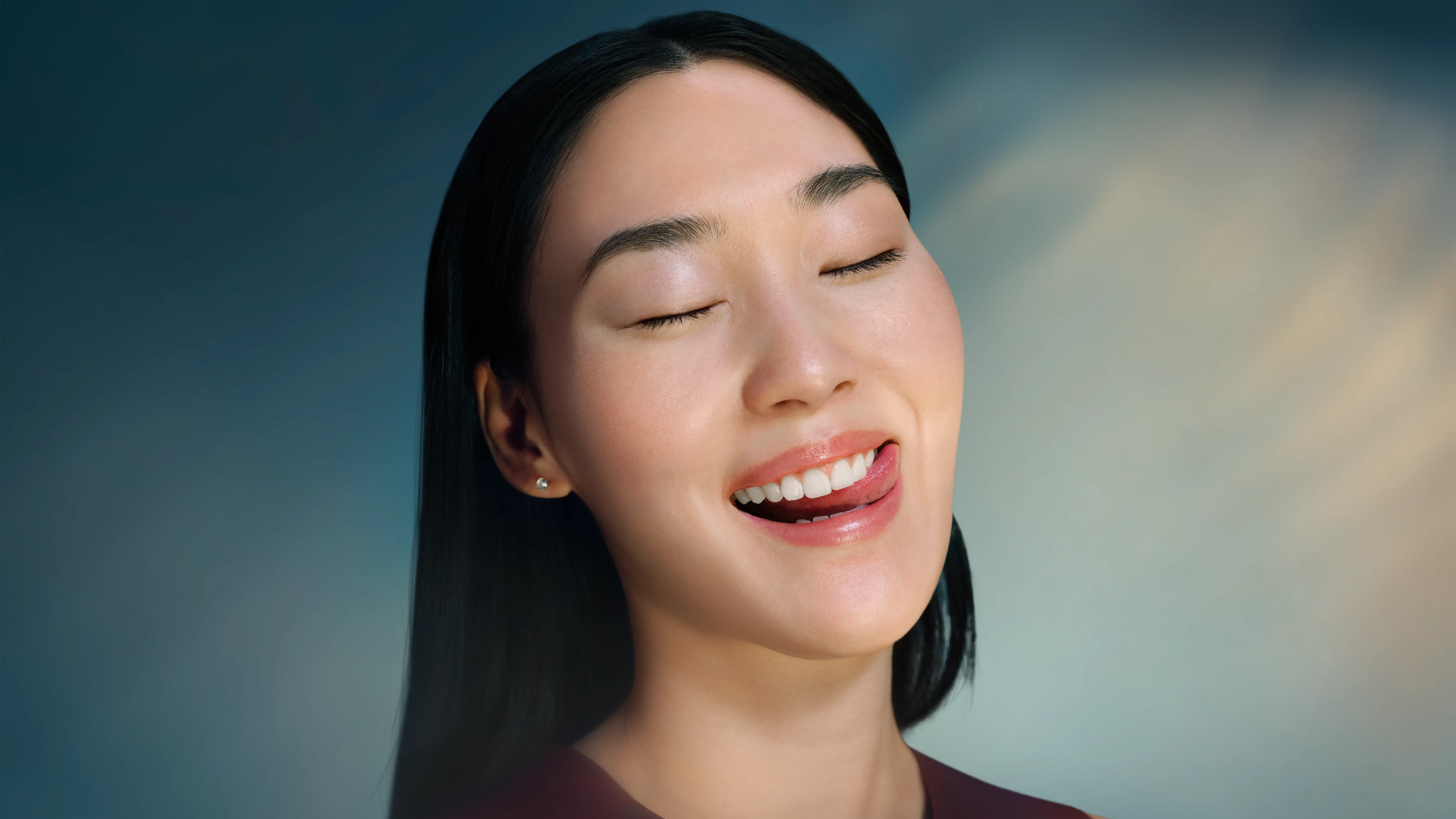 Kobieta z zamkniętymi oczami liże usta na tle niebieskim.