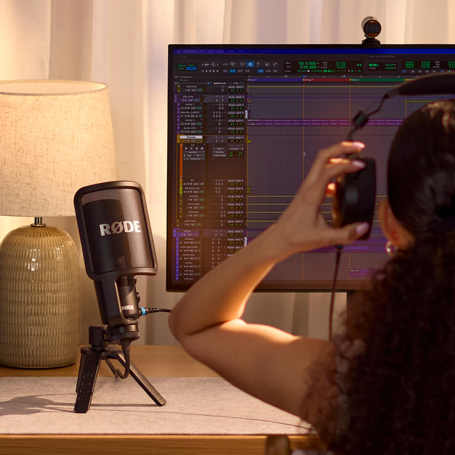 Person with headphones in front of computer monitor showing music software. Rode microphone in foreground.