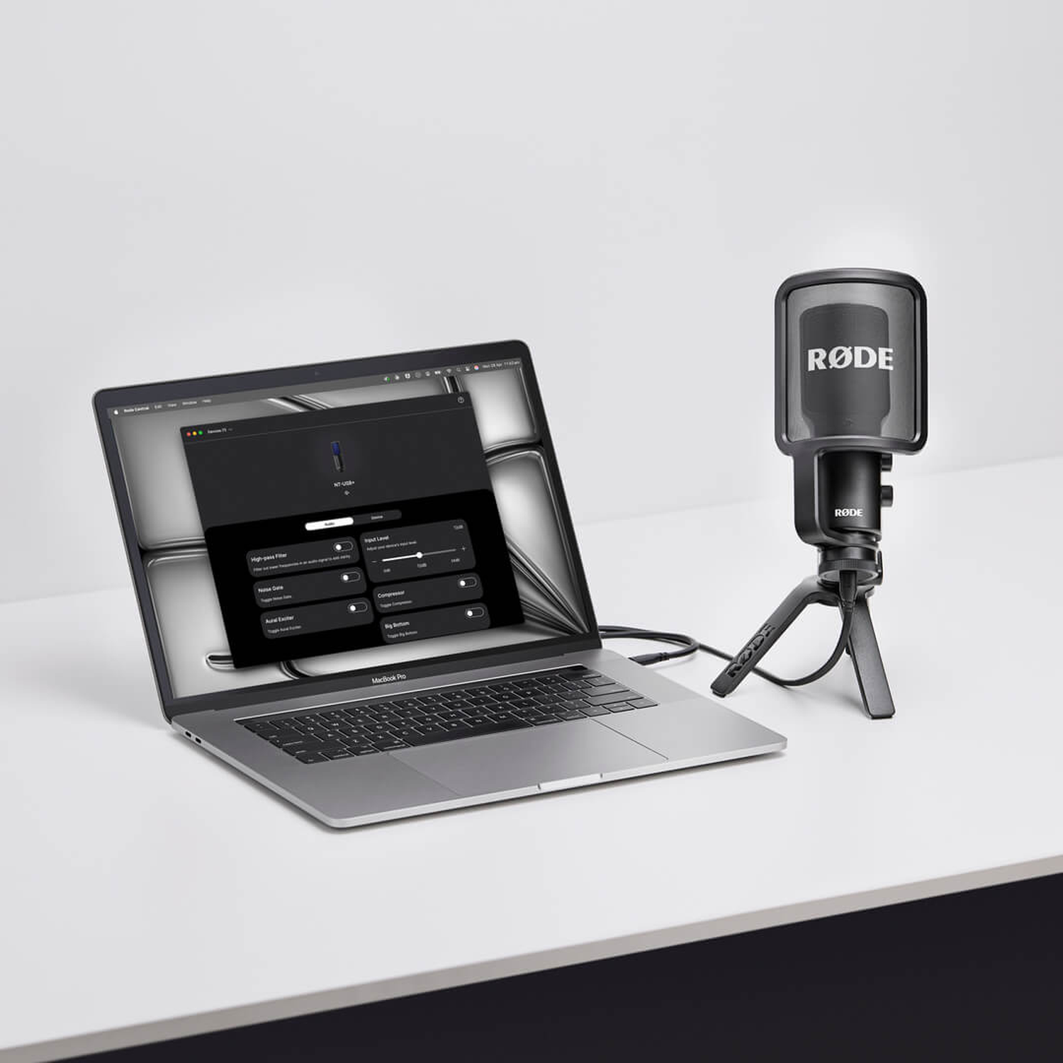 A Rode microphone with a stand next to a MacBook Pro displaying audio software.