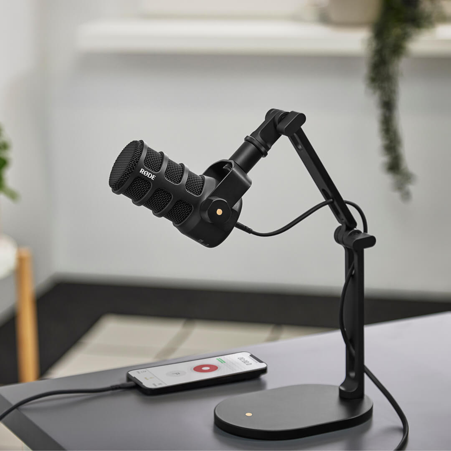 A black microphone on an arm stand sits on a table next to a smartphone.