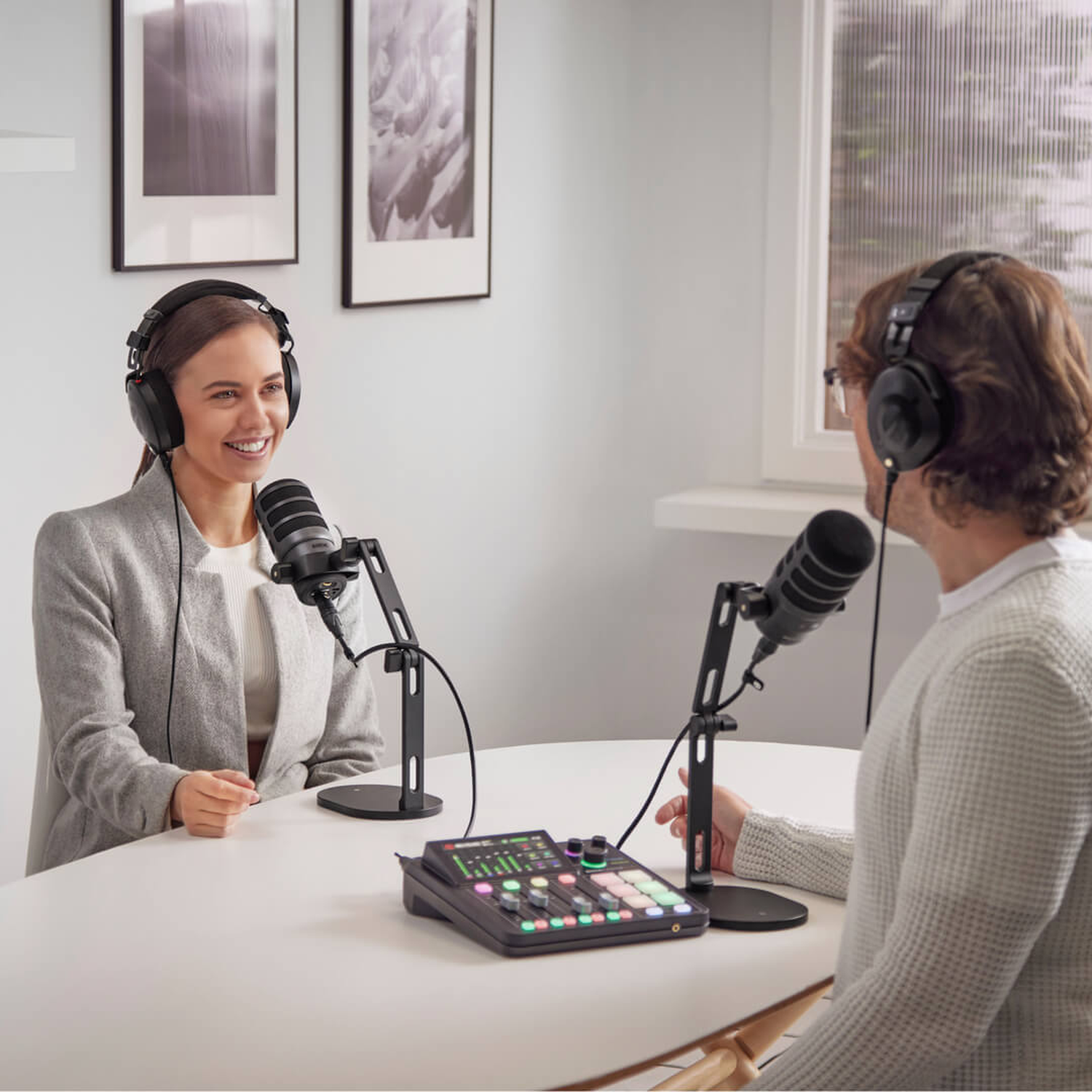Woman and man with headphones at a table with microphones and a mixer for podcasting.