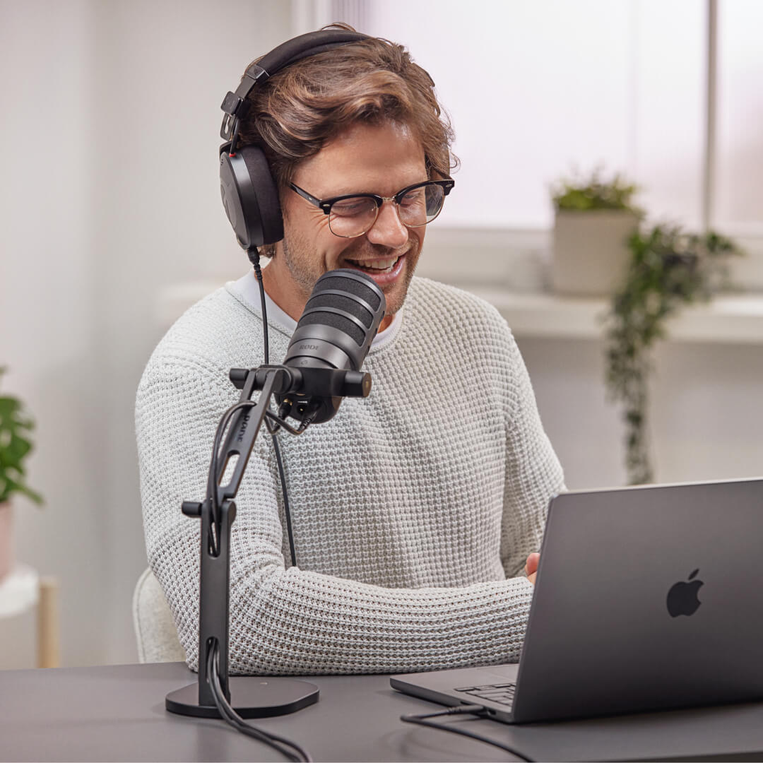 Man with headphones laughs in front of microphone and laptop.