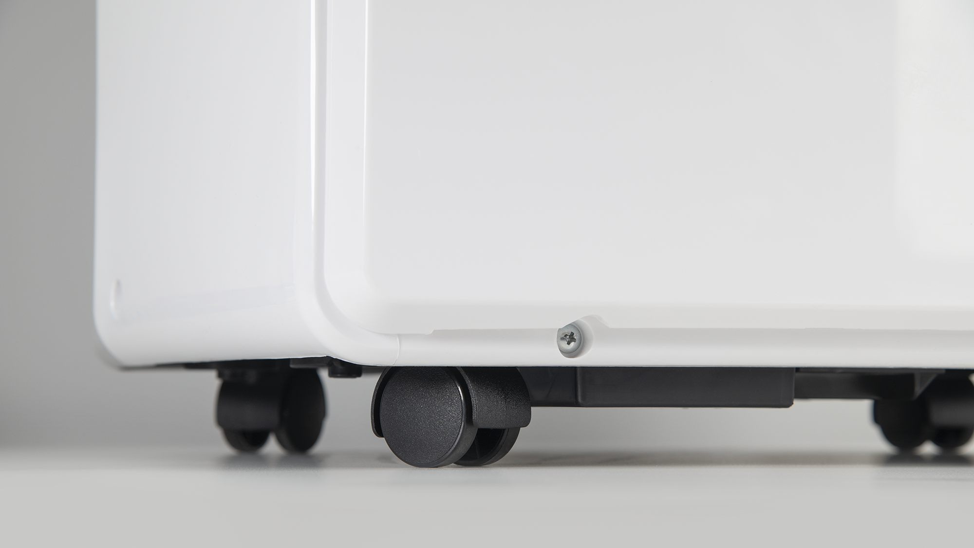 Zbliżenie na dół białego urządzenia z czarnymi kółkami i śrubą.