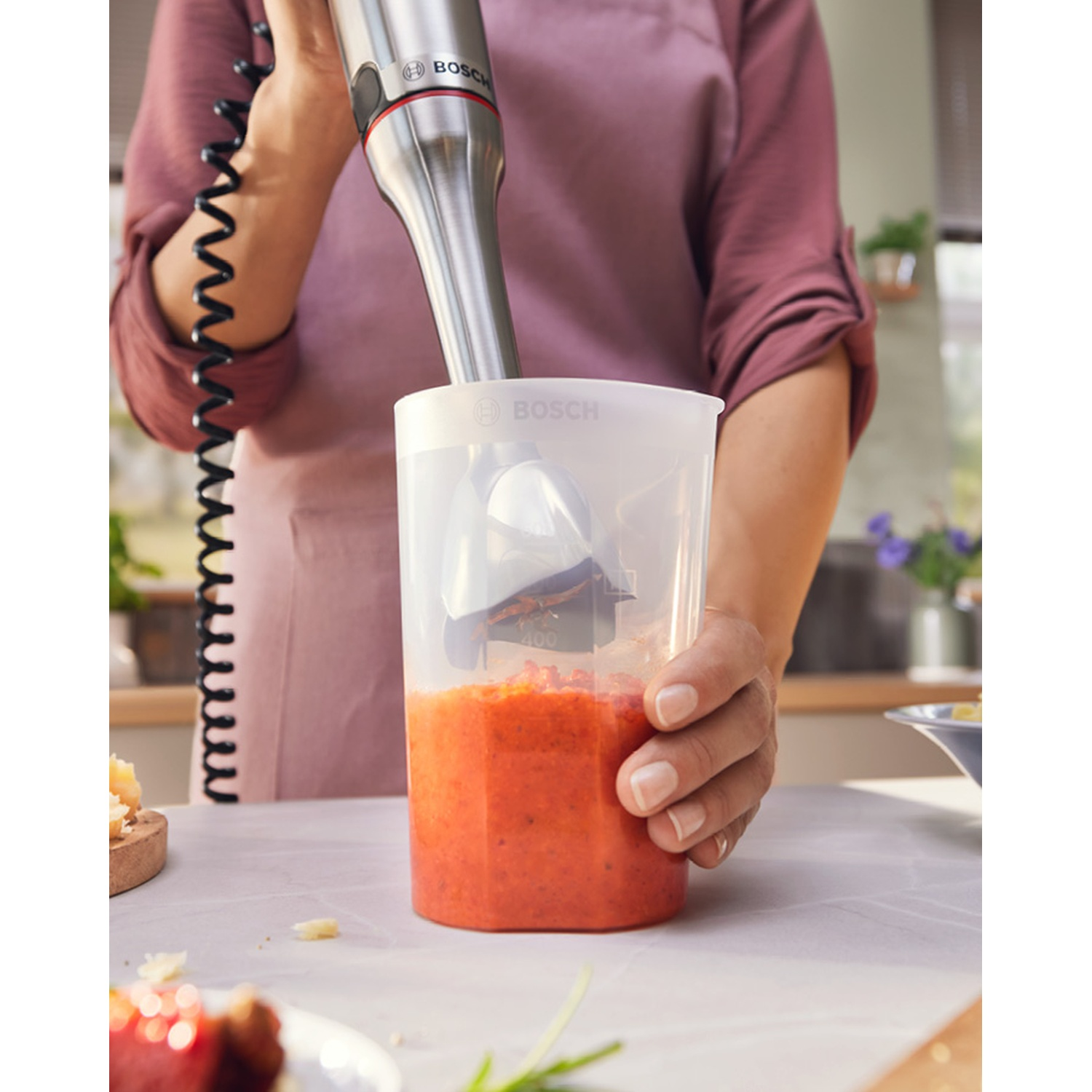 Una persona frulla una salsa rossa in un bicchiere con un frullatore a immersione.