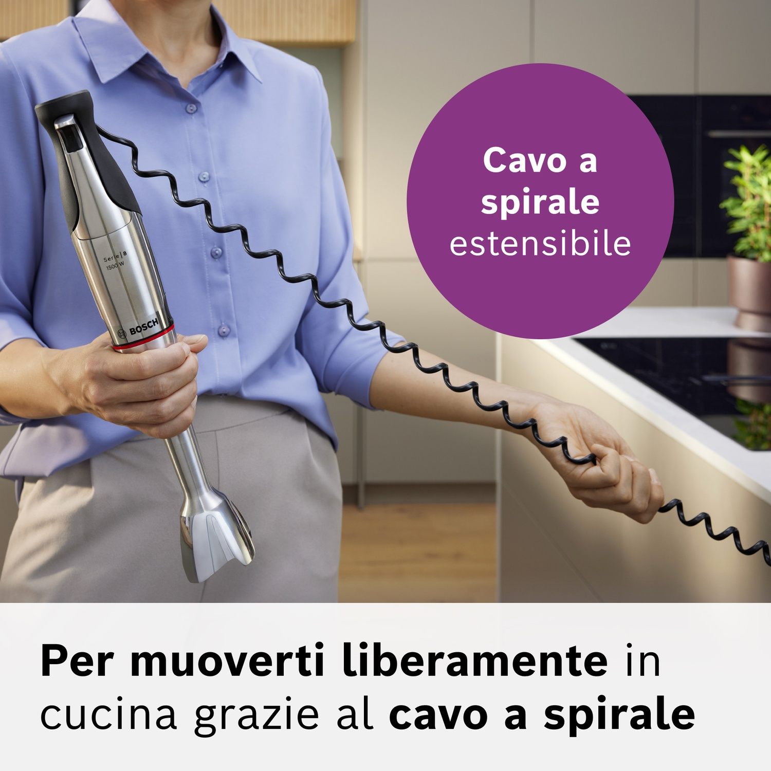 Una persona tiene un frullatore a immersione argentato con cavo a spirale nero in cucina.