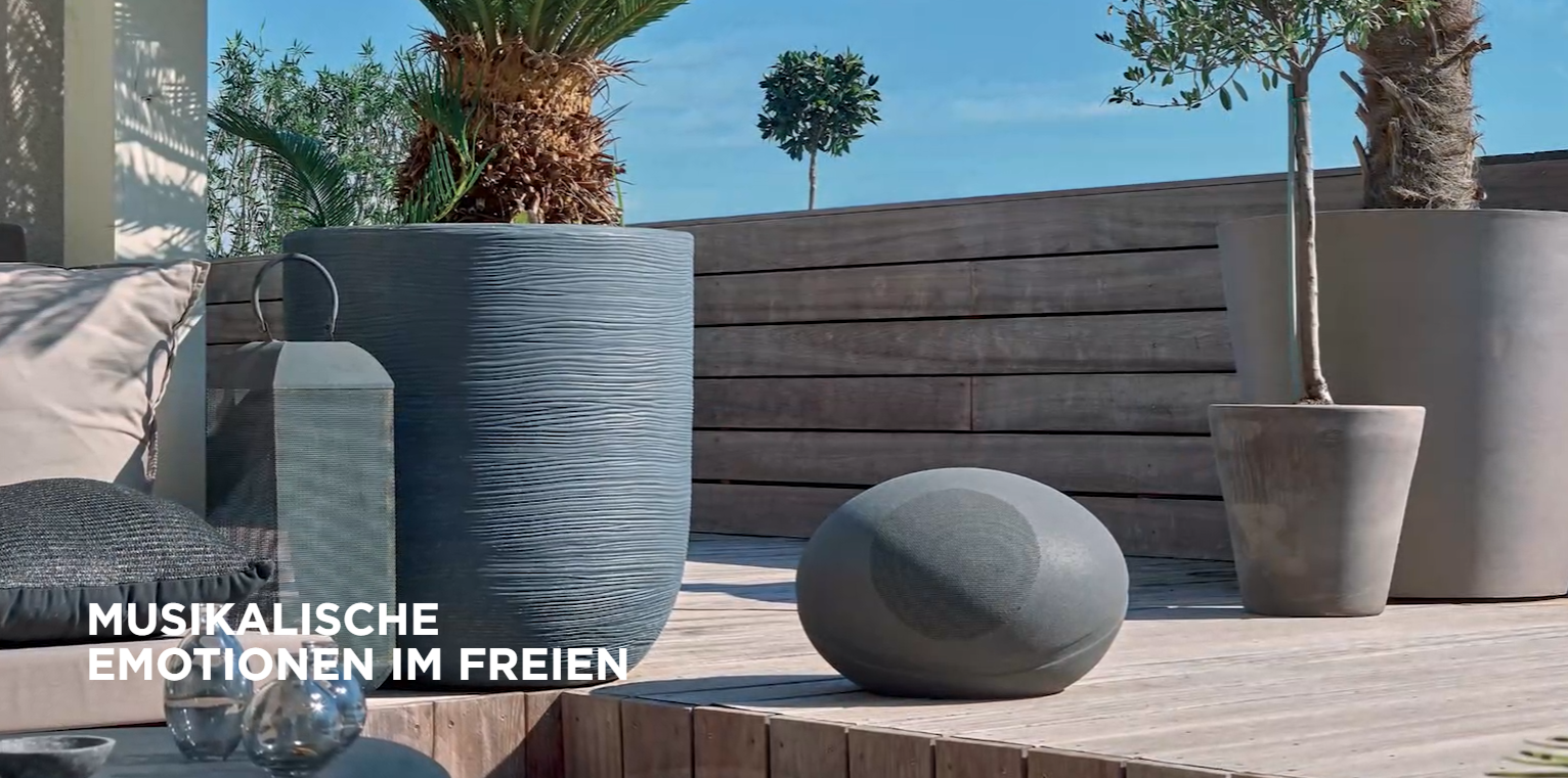 Gartenmöbel mit Pflanzenkübeln, Laterne und Kugellautsprecher auf Holzdeck.