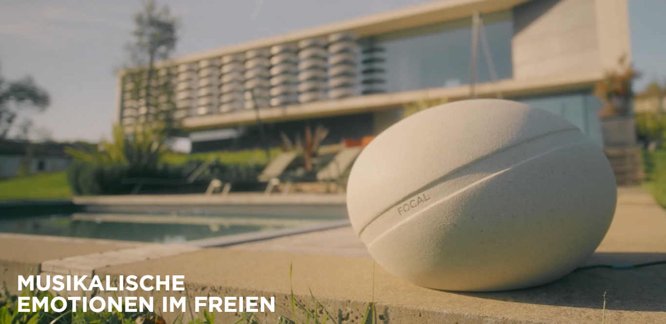 Ein weißer Focal-Lautsprecher steht neben einem Pool vor einem modernen Haus.