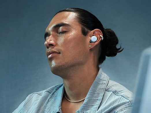 Mężczyzna z zamkniętymi oczami nosi białe słuchawki i naszyjnik.