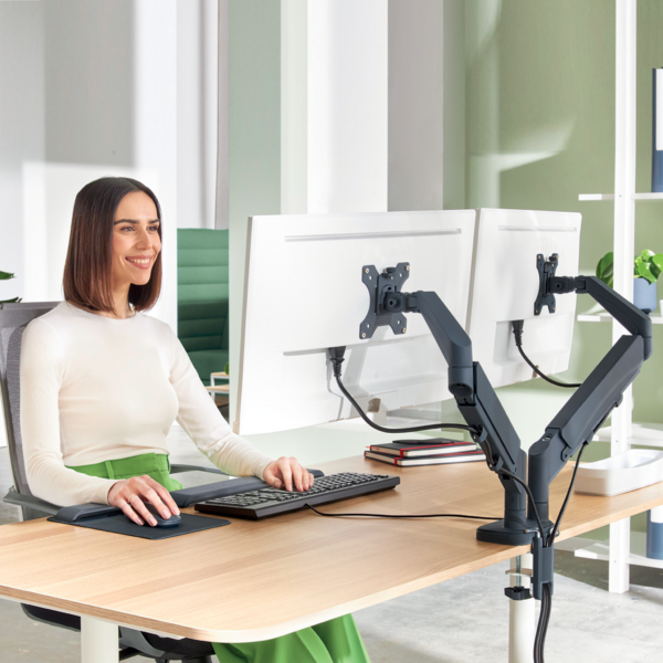 Eine Frau sitzt an einem Schreibtisch mit zwei Monitoren und tippt auf einer Tastatur.