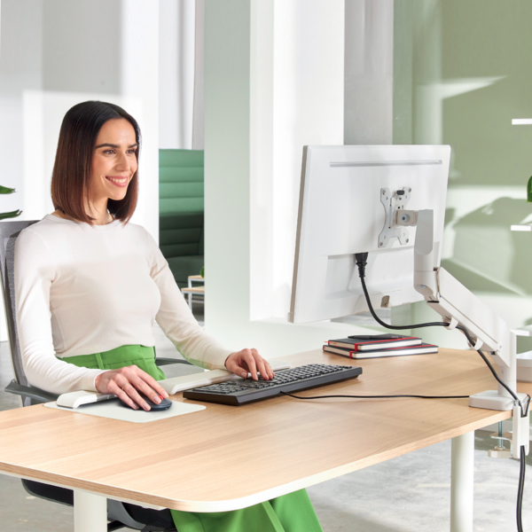 Eine Frau in weißem Oberteil und grünen Rock arbeitet an einem Schreibtisch mit Computer.