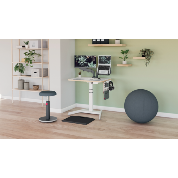 Ein höhenverstellbarer Schreibtisch mit zwei Monitoren, Laptop und Kopfhörern, daneben ein Gymnastikball.