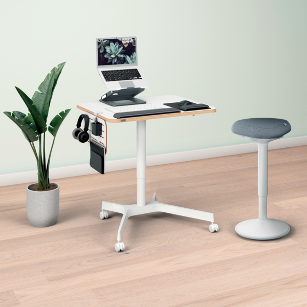 Ein höhenverstellbarer Schreibtisch mit Laptop, Tastatur und Maus, daneben ein Hocker.