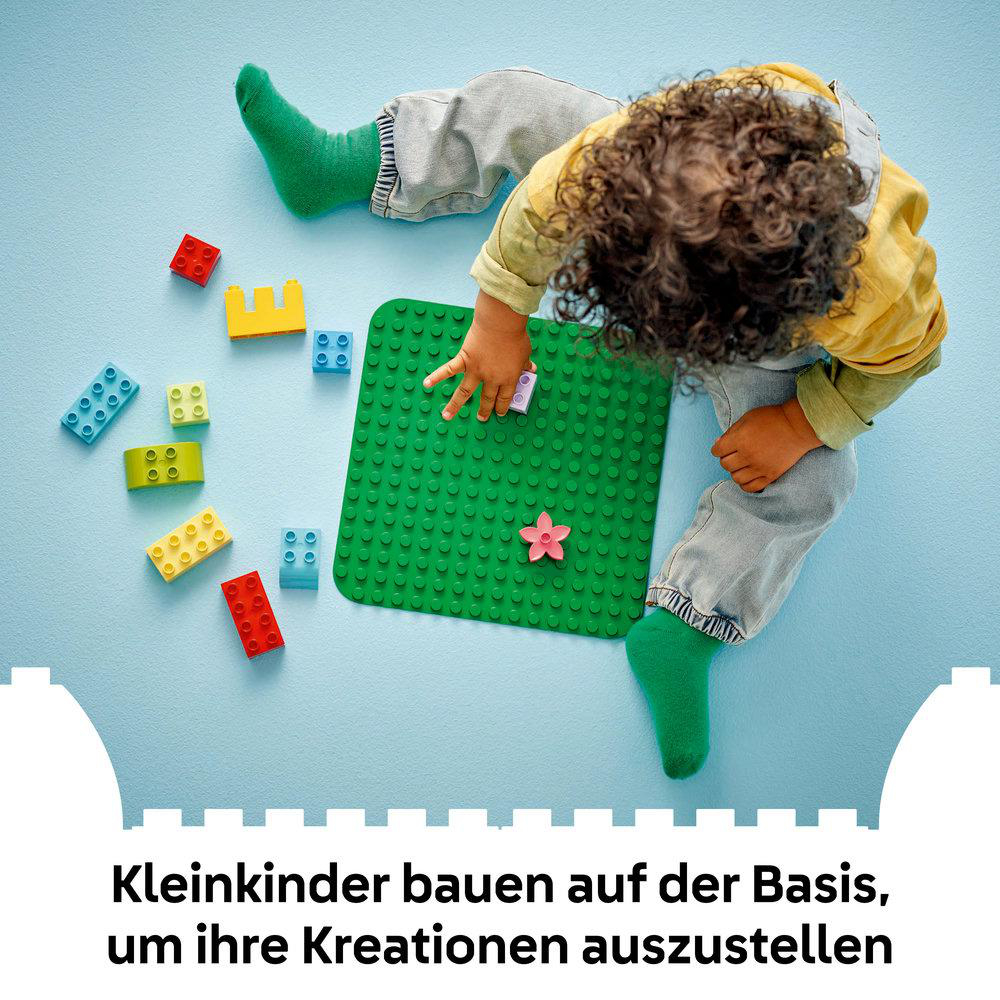Kleinkind mit grünen Socken baut mit bunten Legosteinen auf einer grünen Platte.