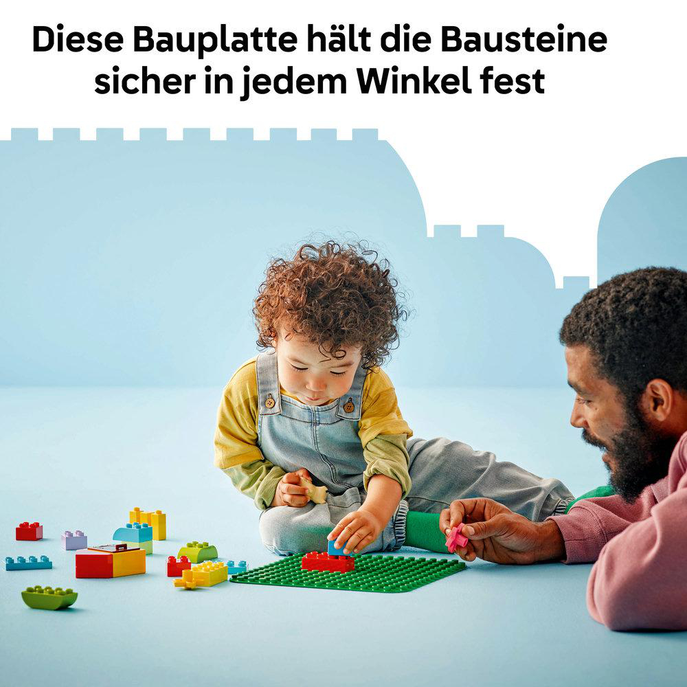 Ein Kind und ein Erwachsener spielen mit bunten Bausteinen auf einer grünen Platte.