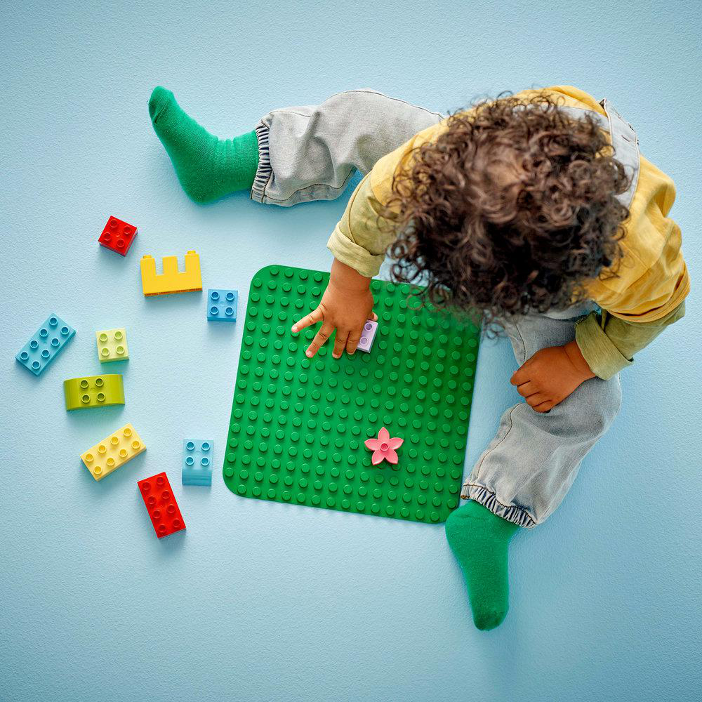 Ein Kind spielt mit bunten Legosteinen auf einer grünen Platte.