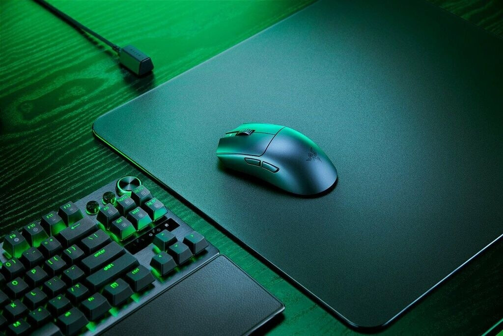 Fekete gamer egér és billentyűzet zöld világítással sötét fán.