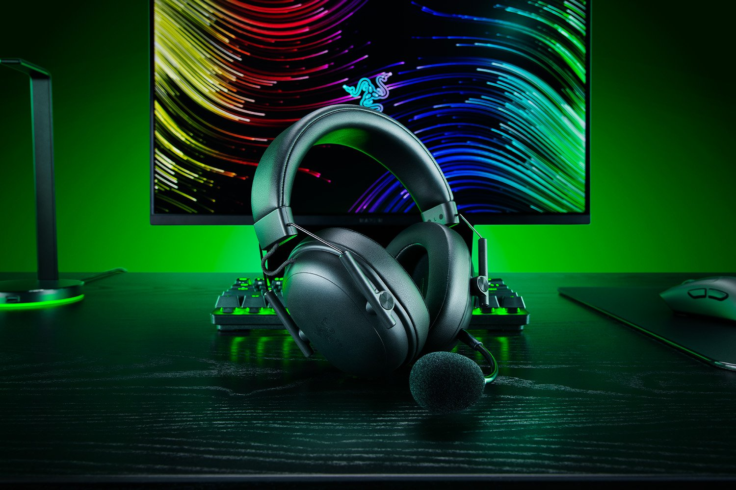 Fekete gamer fejhallgató mikrofonnal, billentyűzet és egér az asztalon.