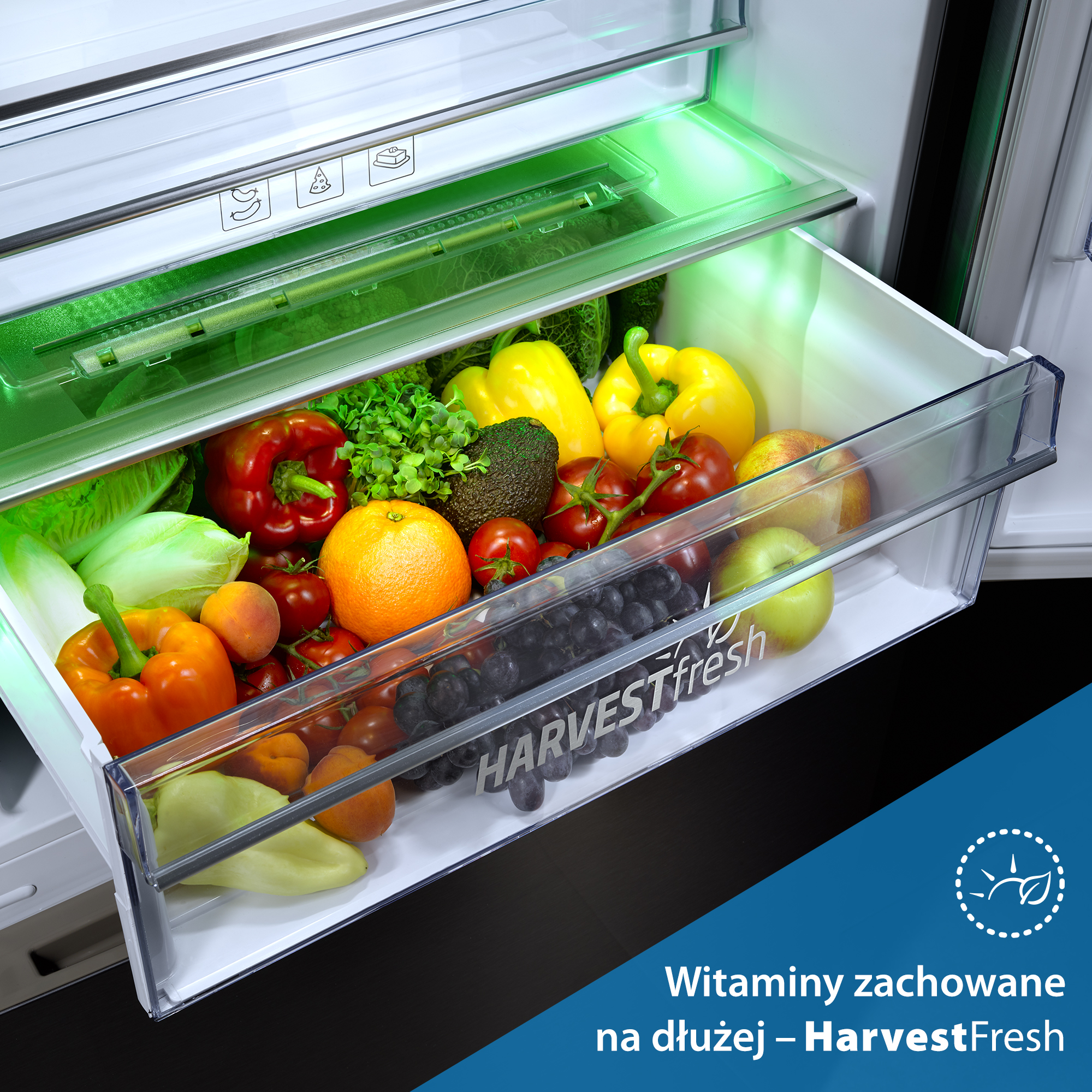 Otwarta szuflada lodówki z owocami i warzywami, oświetlona zielonym światłem.