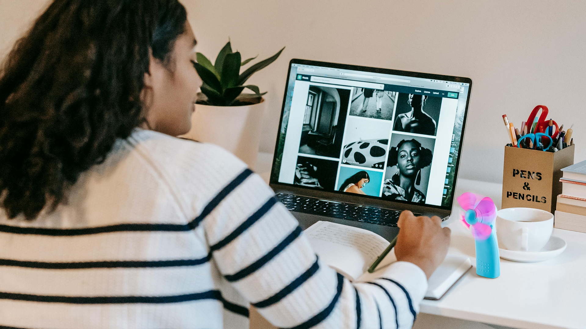 Osoba siedzi przy biurku, patrząc na laptopa wyświetlającego obrazy.