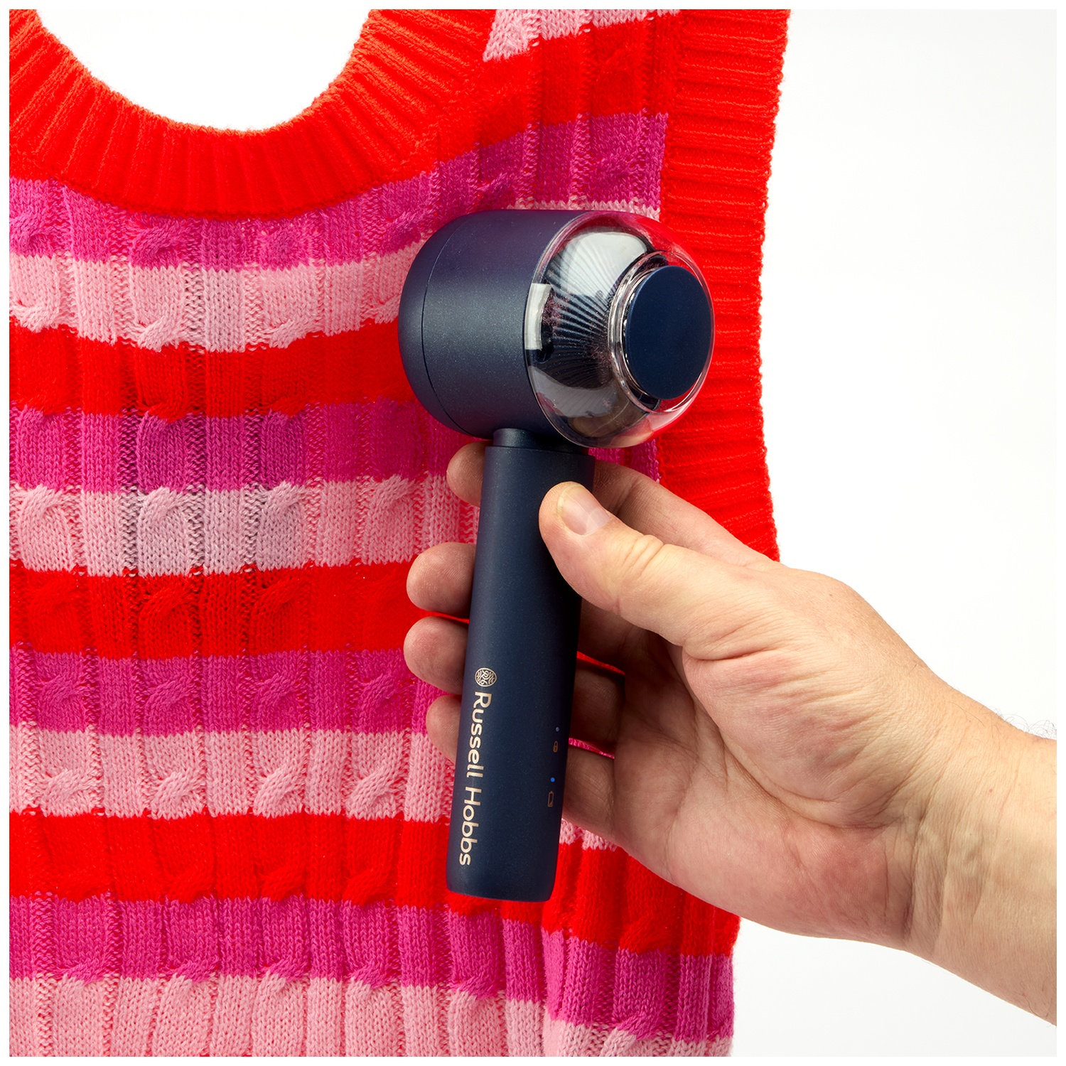 Une main tient un rasoir à tissu bleu foncé près d'un pull à rayures roses et rouges.