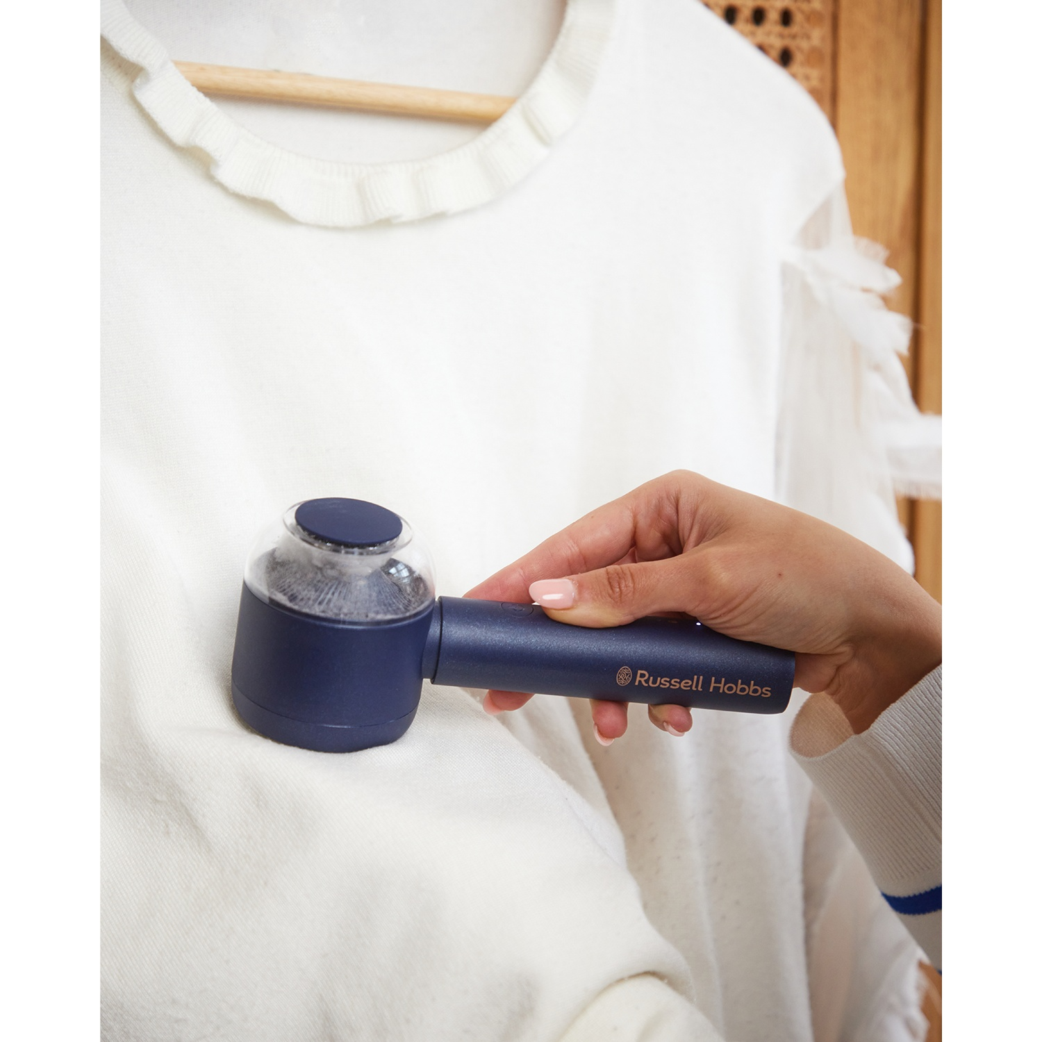 Une main tient un anti-bouloche bleu sur un pull blanc.
