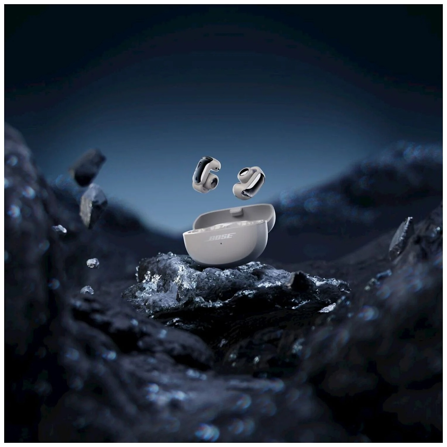 Bose earbuds float above open charging case on dark, wet rocks. Small water droplets.