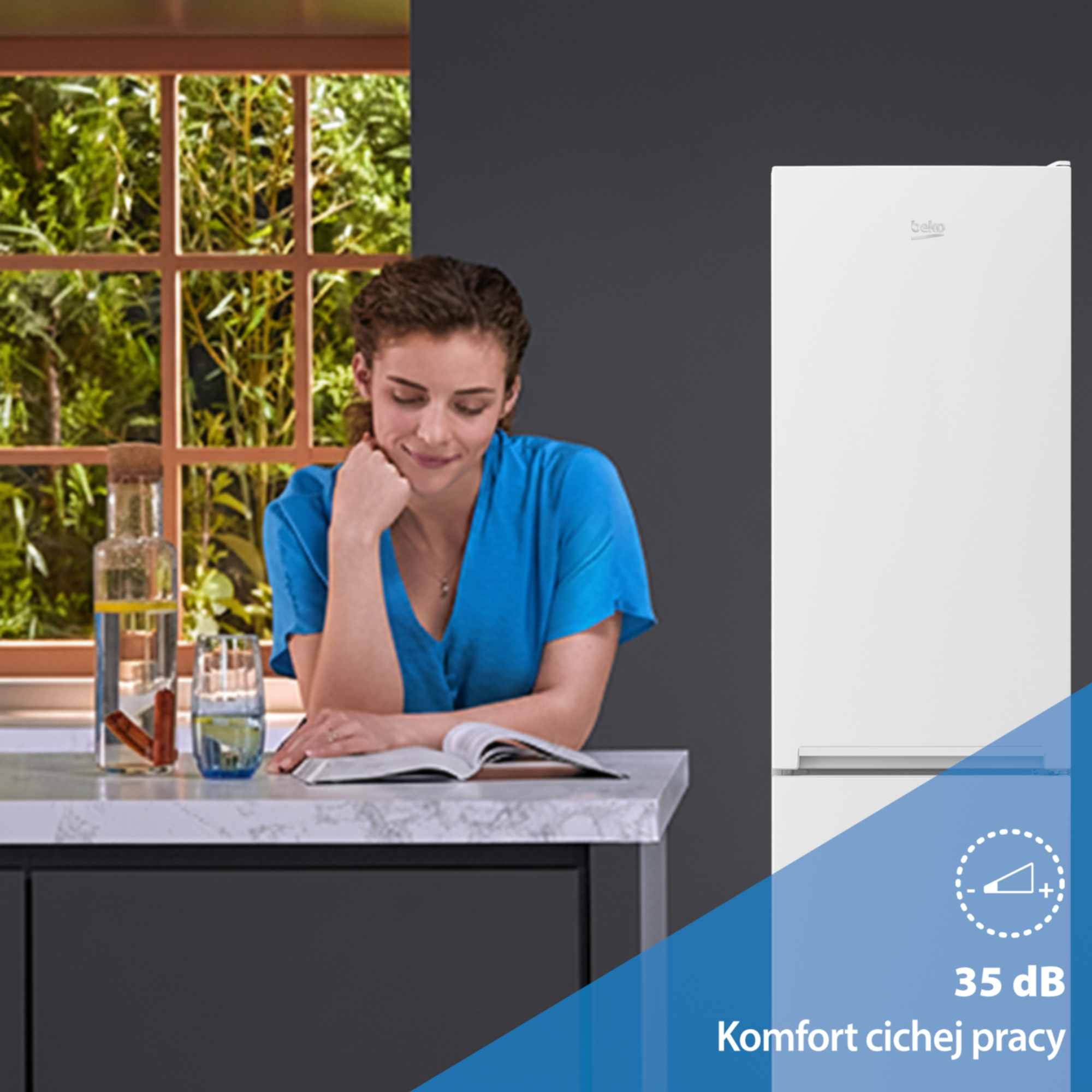 Kobieta czyta książkę obok lodówki z oknem i zielenią w tle.