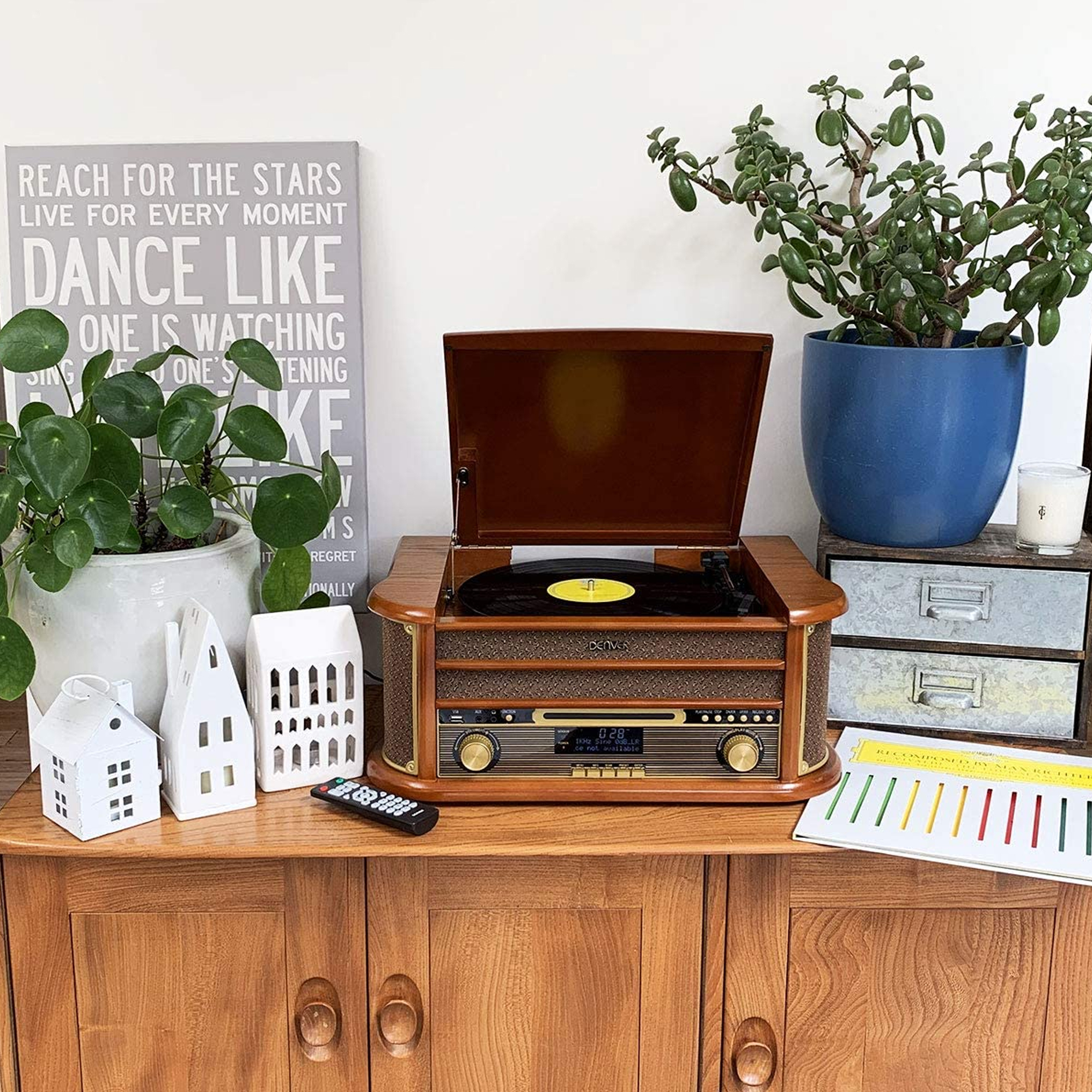 Un giradischi con disco in vinile su un mobiletto di legno con piante e decorazioni.