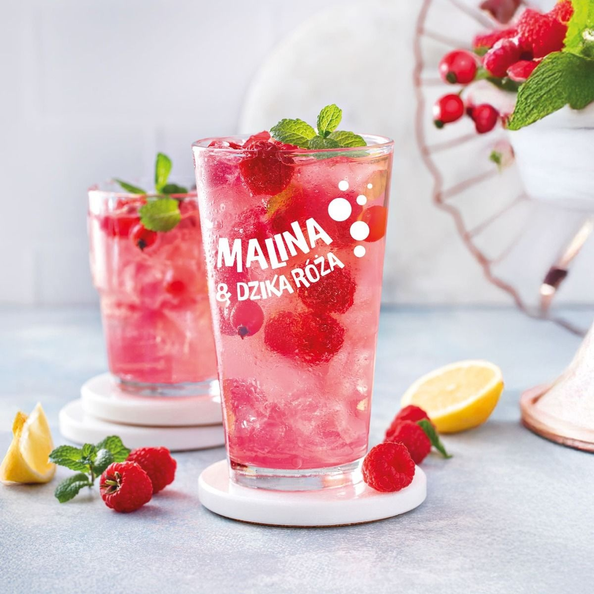 Dwa szklanki różowego napoju z malinami, miętą, cytryną i kostkami lodu.