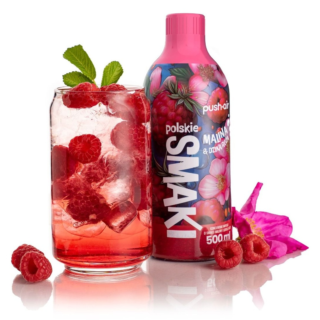 Szklanka napoju malinowego z lodem, obok butelka napoju malinowego z kwiatami.