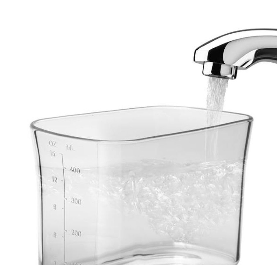 Kran kapie wodą do przezroczystego kubka miarowego wypełnionego wodą.