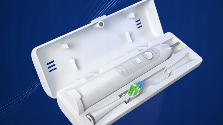 Biała szczoteczka elektryczna w etui ładującym na niebieskim tle.
