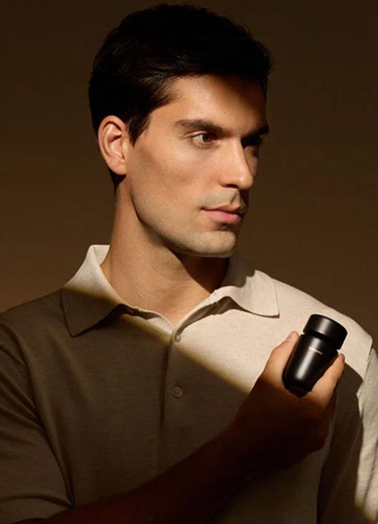 Mężczyzna w koszulce polo trzyma czarną buteleczkę. Pada na niego światło.