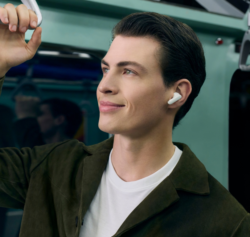 Mężczyzna z białymi słuchawkami trzyma się poręczy w pociągu.