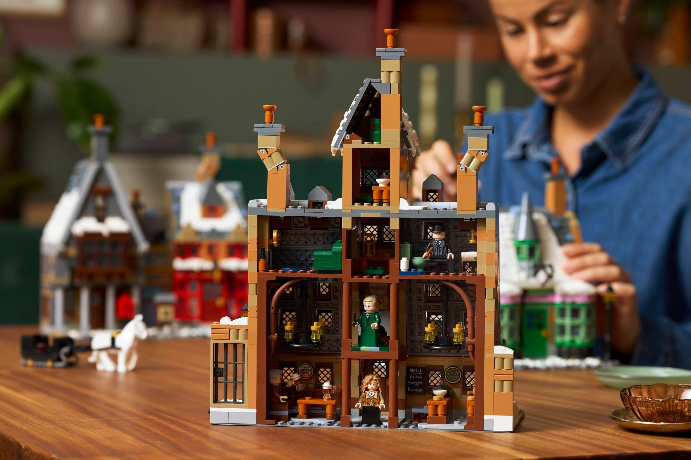 Model domu z klocków Lego z figurkami i zaprzęgiem konnym na pierwszym planie.